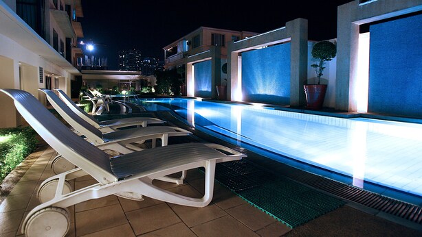 An outdoor swimming pool area with lounge chairs and a well-lit pool. - Astoria Plaza (Pasig)