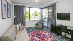 A modern living room with a sofa, a patterned rug, a desk, and a television. - East Perth Suites Hotel (East Perth)