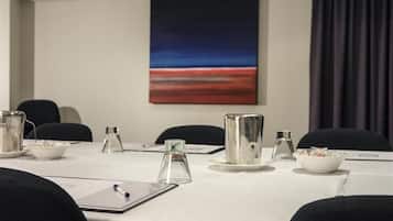 Un salón de conferencias con una mesa blanca, sillas, un cuadro en la pared y una ventana con cortinas.