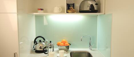 A modern kitchen with a stainless steel sink, a kettle, a coffee maker, and a bowl of oranges.