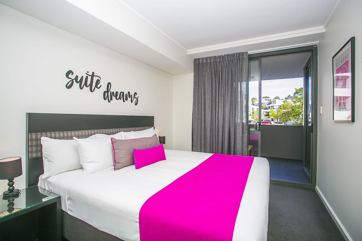 A hotel room with a bed, a nightstand, a window with curtains, and a wall sign that reads "suite dreams".