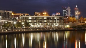 A waterfront hotel with modern architecture, a reflection pool, and a city skyline in the background. - East Perth Suites Hotel (East Perth)