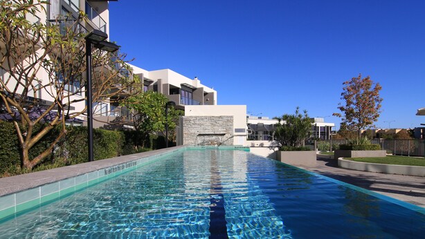 A swimming pool with clear blue water, surrounded by modern buildings and greenery. - East Perth Suites Hotel (East Perth)