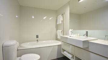 A modern bathroom with a bathtub, a toilet, and a vanity with a mirror.