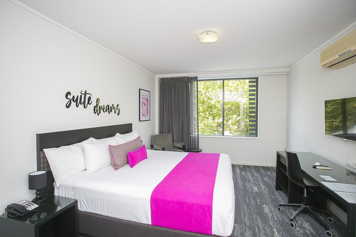 A hotel room with a bed, a desk, a chair, a telephone, and a window with curtains.