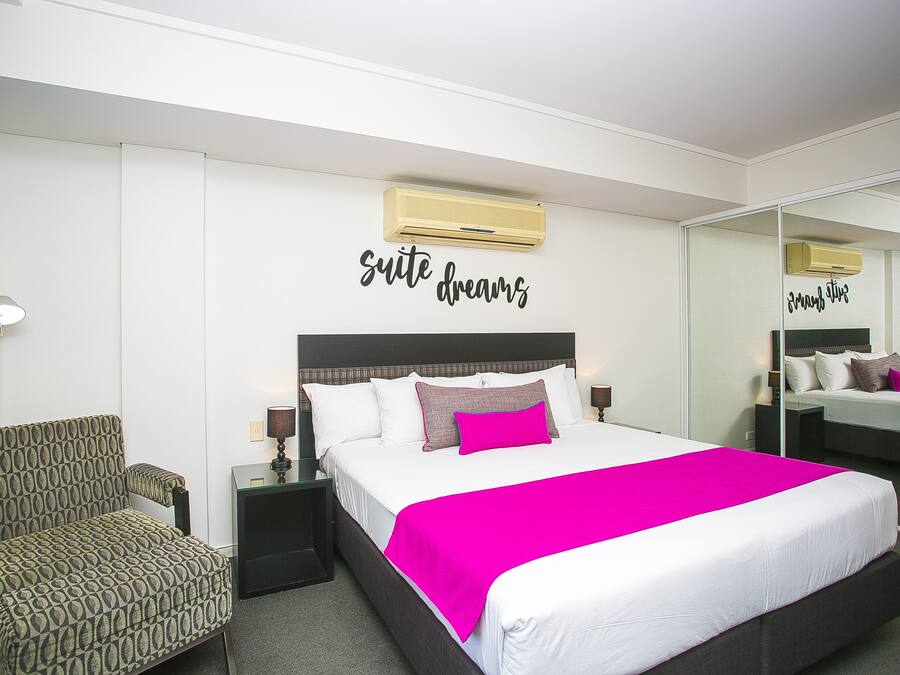 Una habitación de hotel con cama, una silla, una mesita de noche y un espejo.