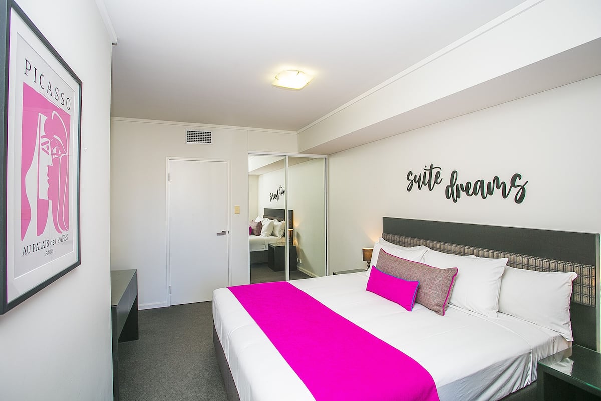 A hotel room with a bed, a mirror, a nightstand, and a wall with a 'suite dreams' sign.