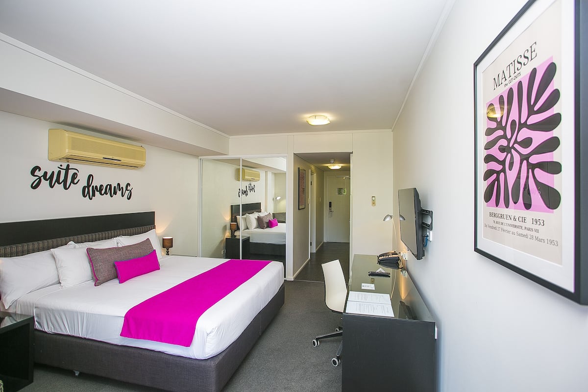 A hotel room with a large bed, a desk, and a chair. There is a mirror on the wall and a framed picture of a painting.