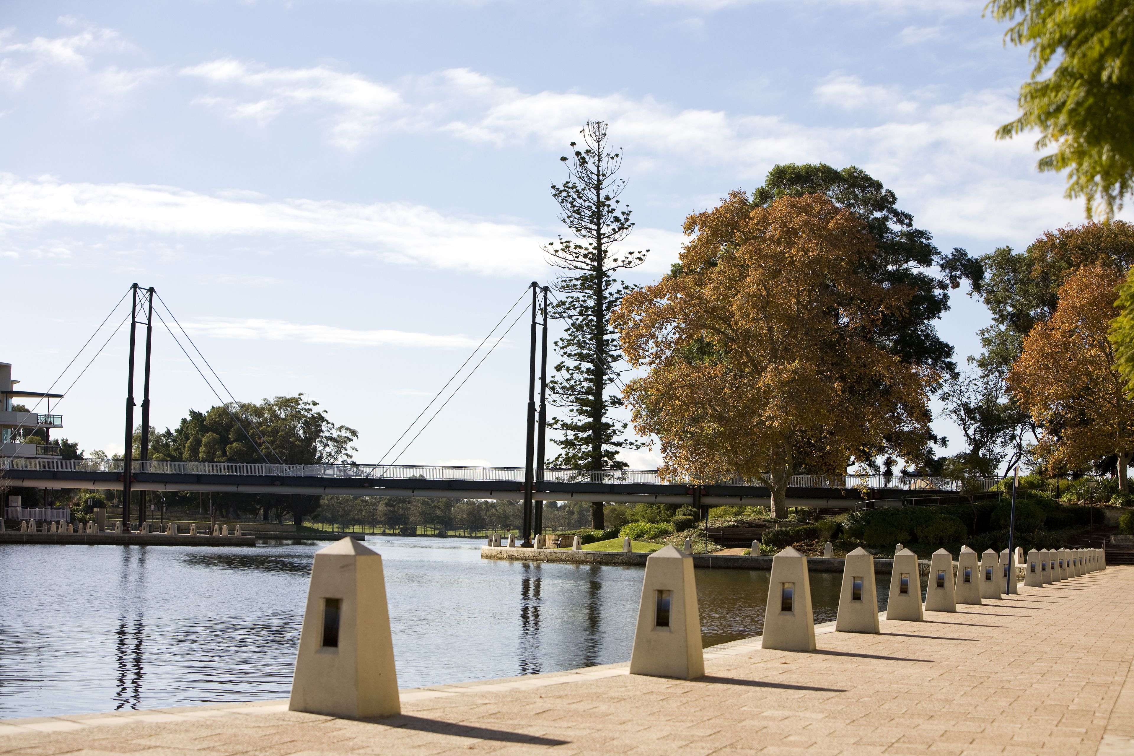 A riverside walkway with a bridge in the background, featuring a series of bollards along the path.