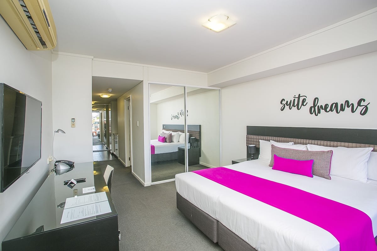 A hotel room with a bed, a desk, a mirror, and a wall with the text "suite dreams".
