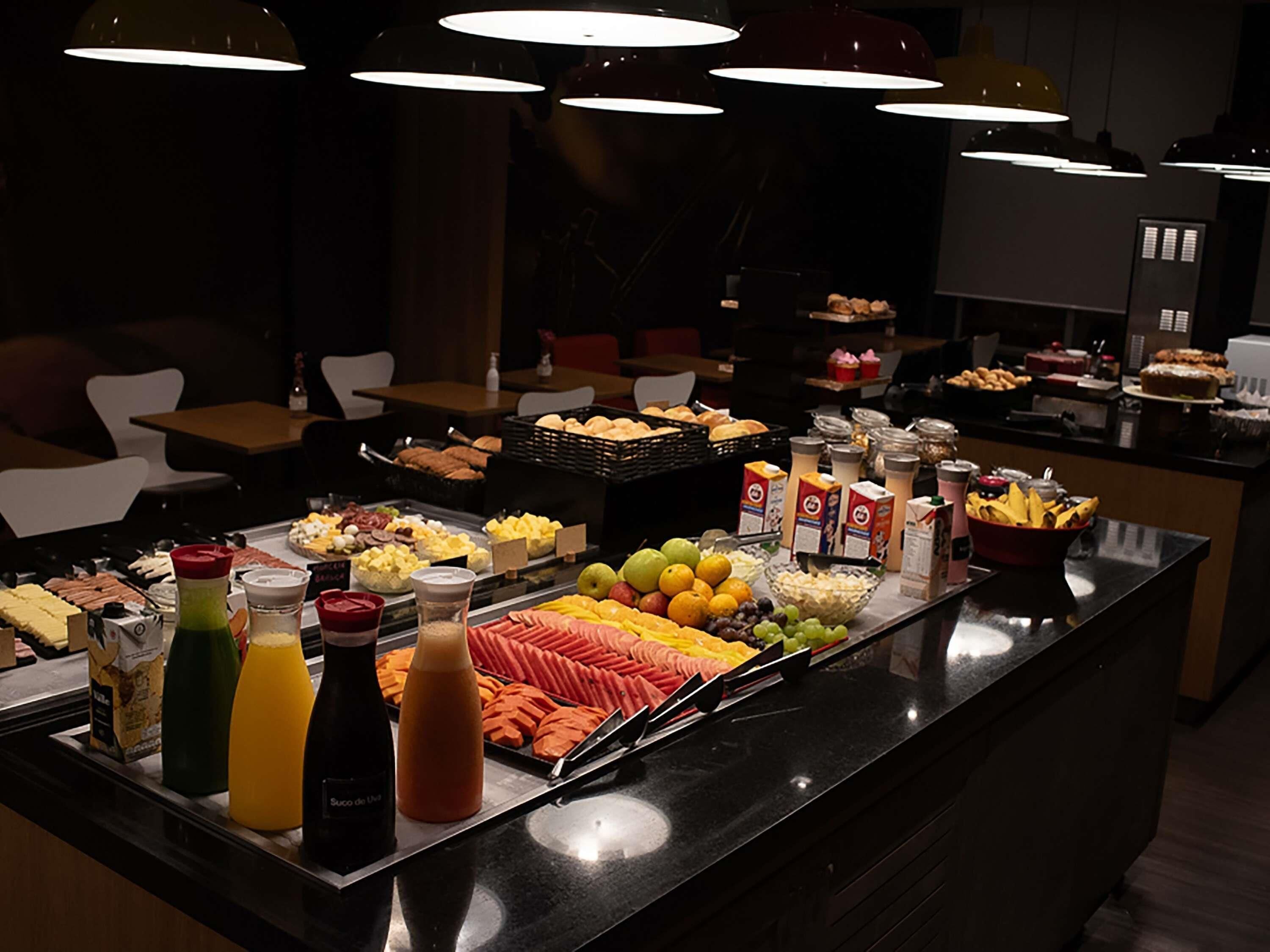 Buffet com diversas opções de comida e bebidas, incluindo frutas, carnes e produtos lácteos.