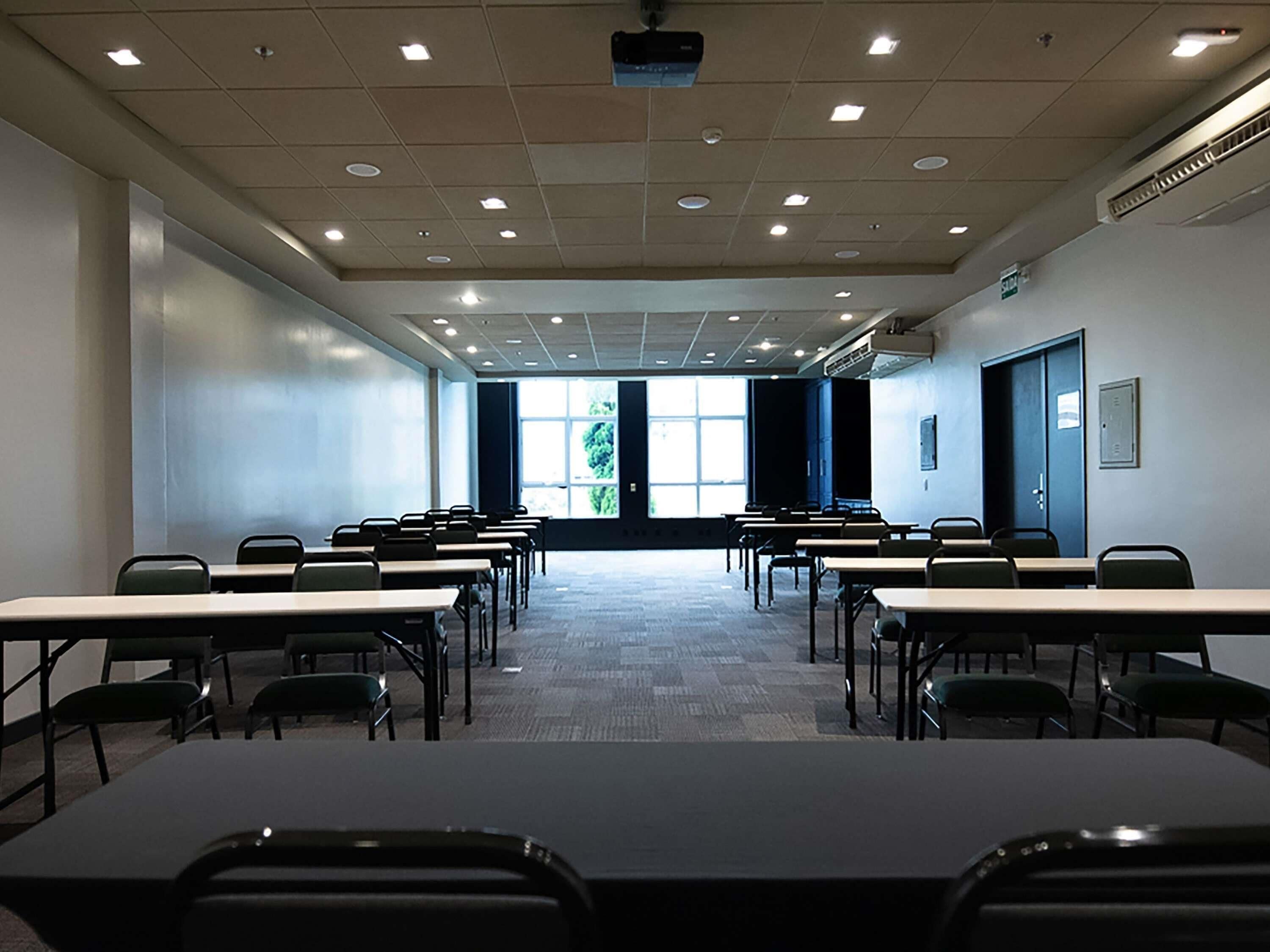 A conference room with multiple tables and chairs, a projector, and large windows.