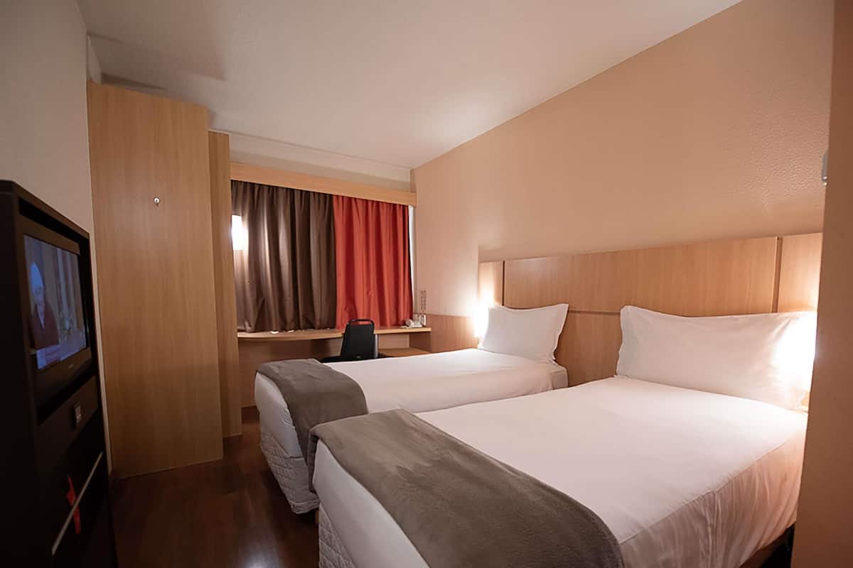 A hotel room with two beds, a desk with a chair, a television, and a window with curtains.