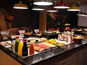 Een buffet met diverse gerechten en drankjes, een bar met uitgestelde dranken, en een zithoek met stoelen en tafels.