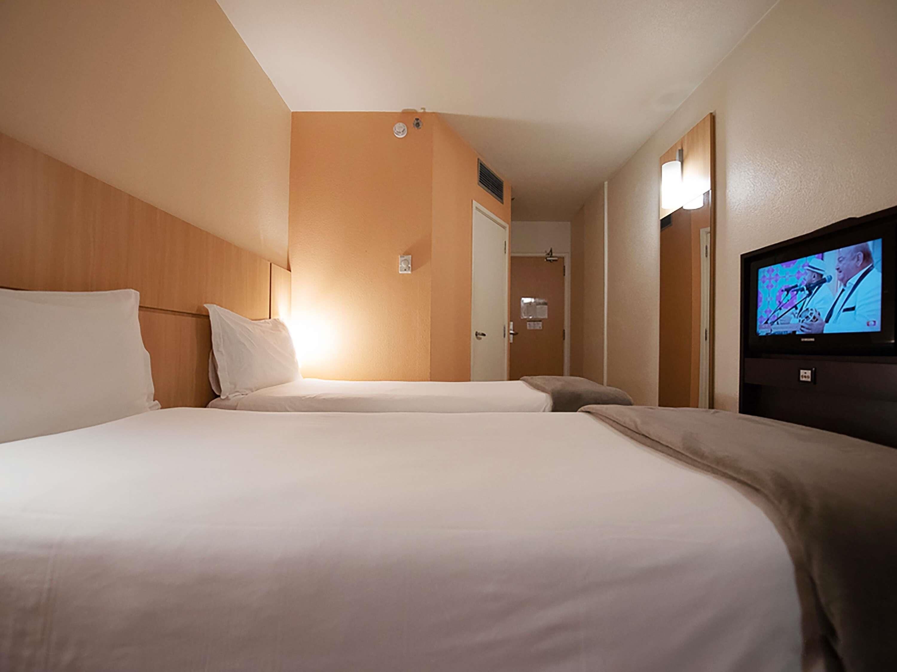 Ein Hotelzimmer mit zwei Betten, einem Fernseher und einer Tür zu einem Badezimmer.
