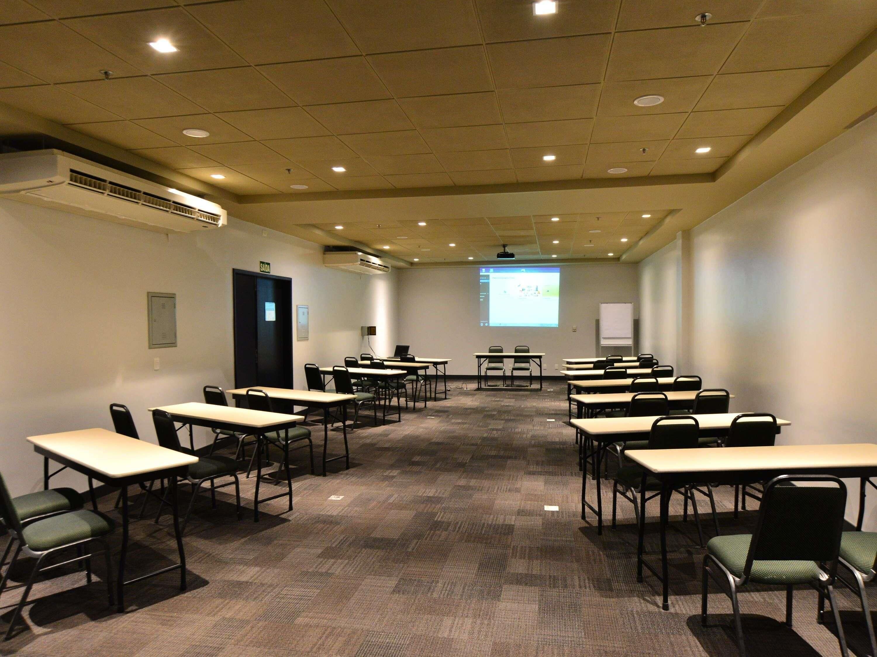 Een vergaderzaal met meerdere tafels en stoelen, een scherm voor een beamer en een whiteboard.