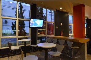 Un moderno espacio de bar con televisor, diversas opciones de asientos y grandes ventanales que ofrecen vistas al exterior.