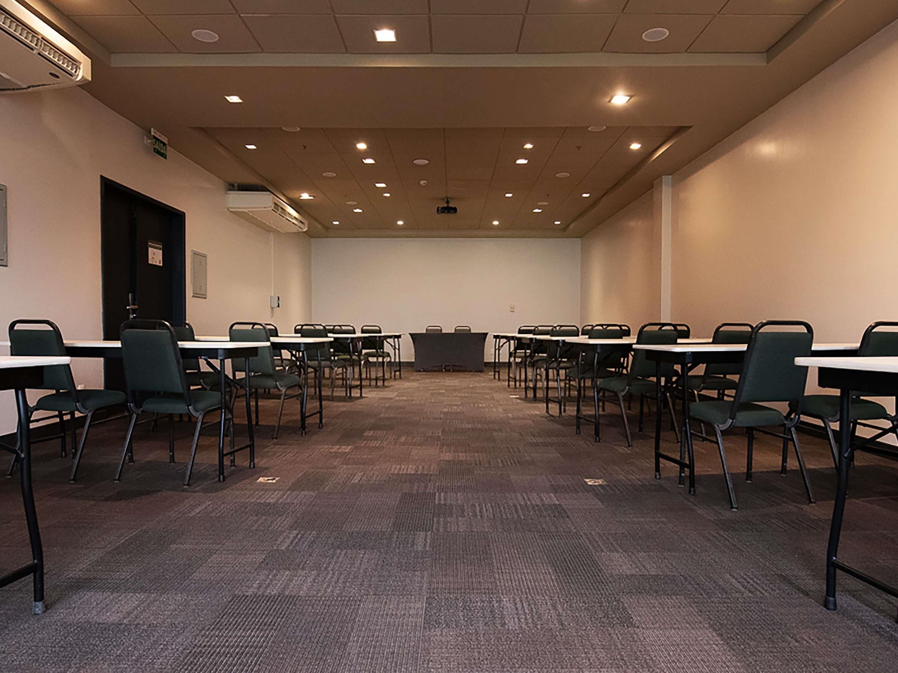 Un salón de conferencias con varias mesas y sillas, un proyector y suelo alfombrado.
