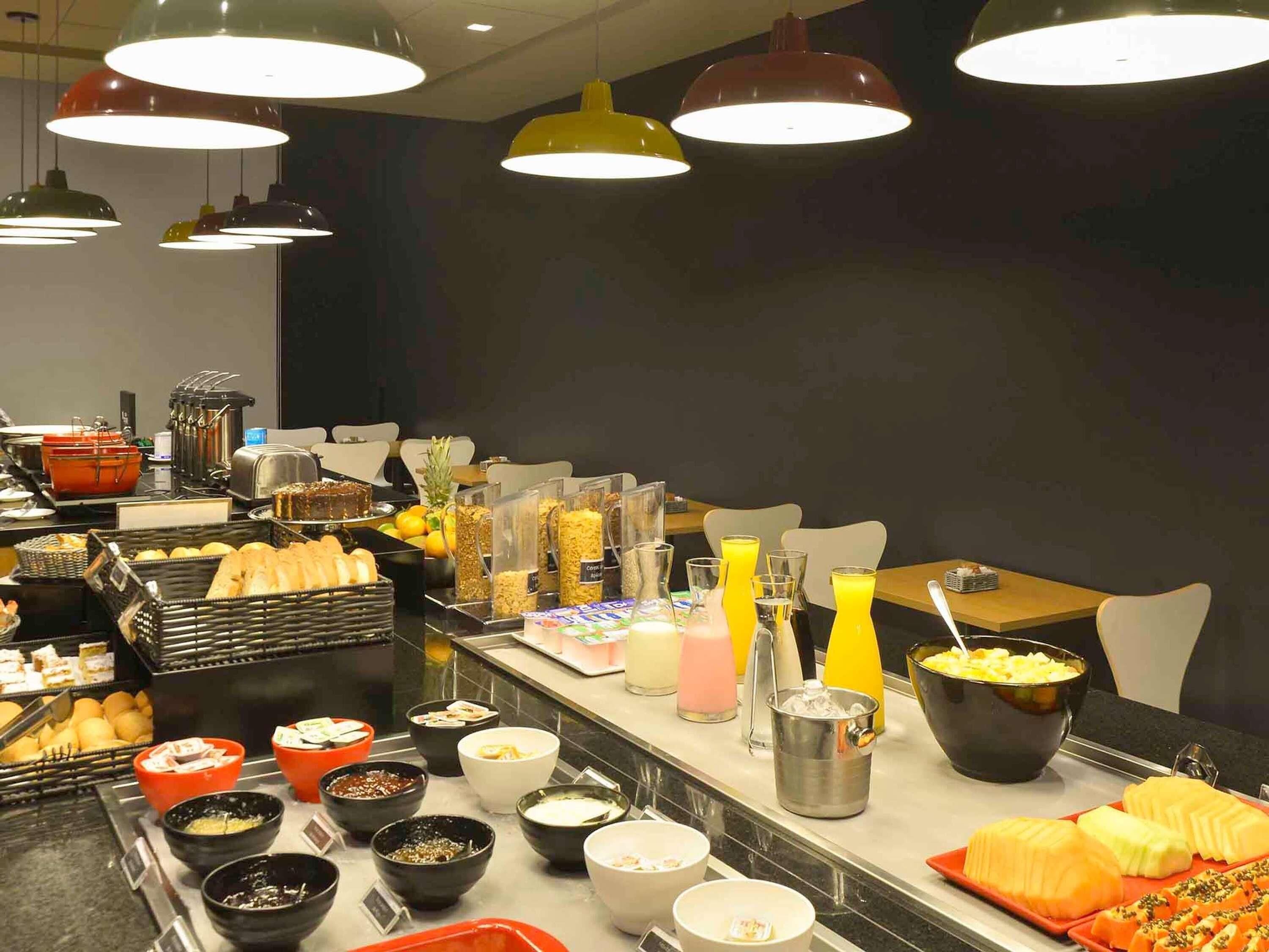 A buffet with various food items and beverages, including fruits, bread, and condiments.