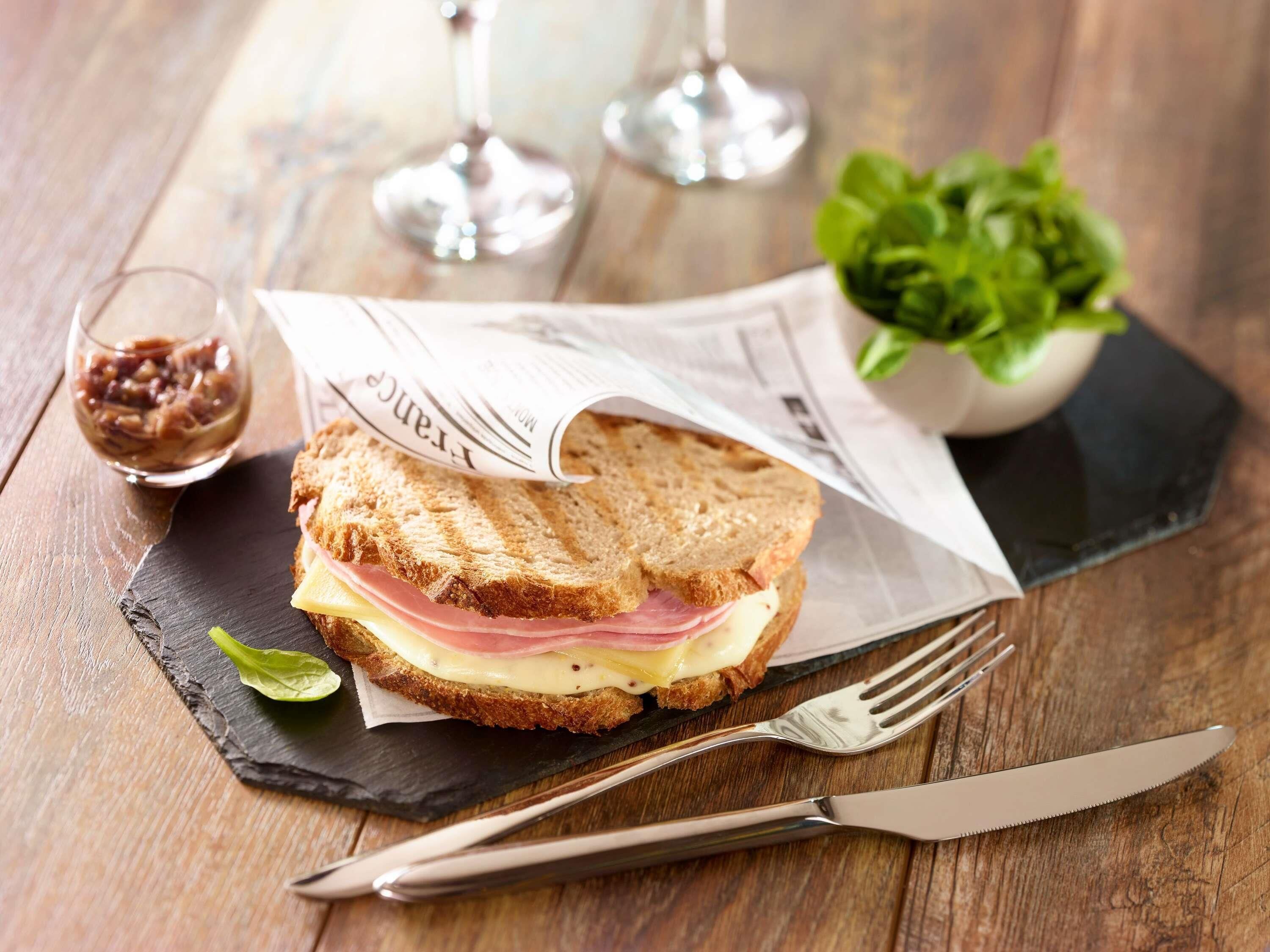 A sandwich on a slate board with a fork and knife beside it.