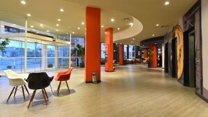 A modern lobby with a curved ceiling, large windows, and a seating area with three chairs.