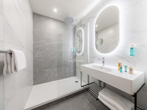 A modern bathroom with a glass-enclosed shower, a white sink with a mirror, and a towel rack. - Novotel Paris 13 Porte d'Italie (Le Kremlin-Bicetre)