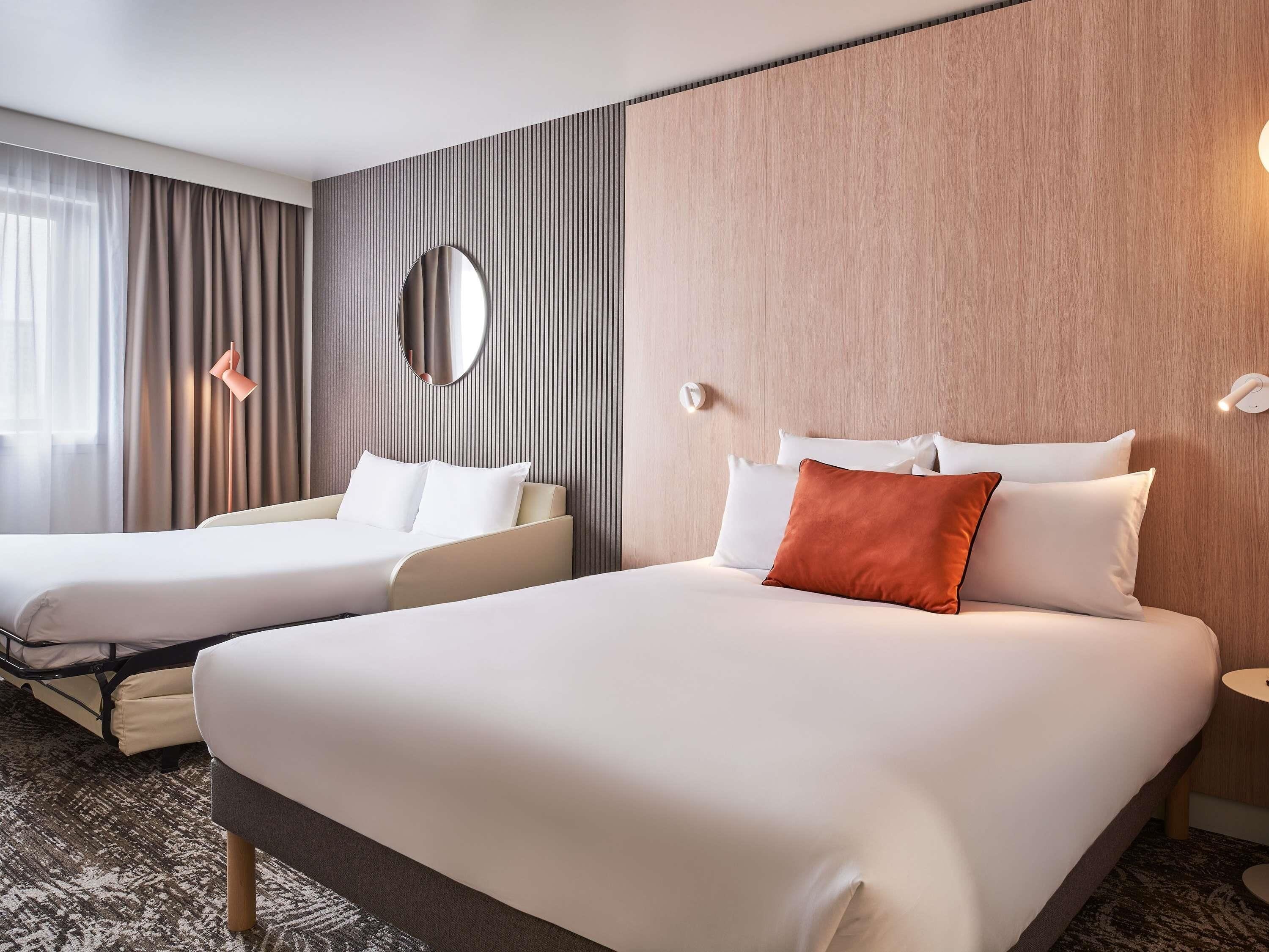 Une chambre d’hôtel avec deux lits, un grand miroir, une lampe de chevet et un luminaire fixé au mur.
