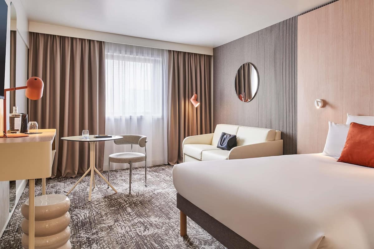Una habitación de hotel con una cama, un escritorio, una silla, una mesa redonda y un espejo.