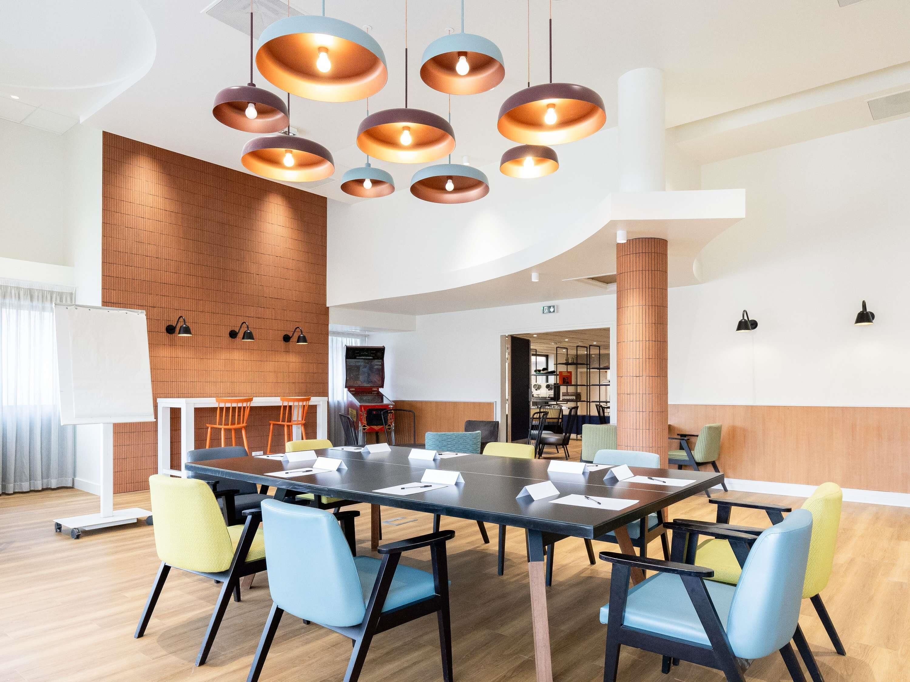 Une salle de réunion moderne, dotée d’une longue table, de nombreuses chaises et d’un éclairage suspendu.