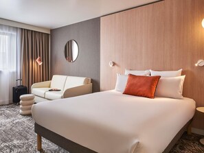 Een hotelkamer met een groot bed, een slaapbank, een ronde spiegel en een nachtkastje.