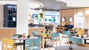 A modern restaurant with round tables and chairs, a bar area with shelves of bottles, and a seating area with a teddy bear. - Novotel Paris 13 Porte d'Italie (Le Kremlin-Bicetre)