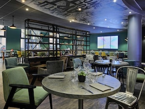 A restaurant interior with round tables, chairs, and a high ceiling with exposed beams and lighting fixtures.