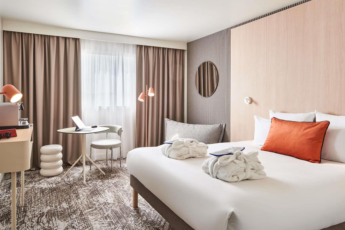 Una habitación de hotel con cama, escritorio, silla, espejo redondo y una mesita.