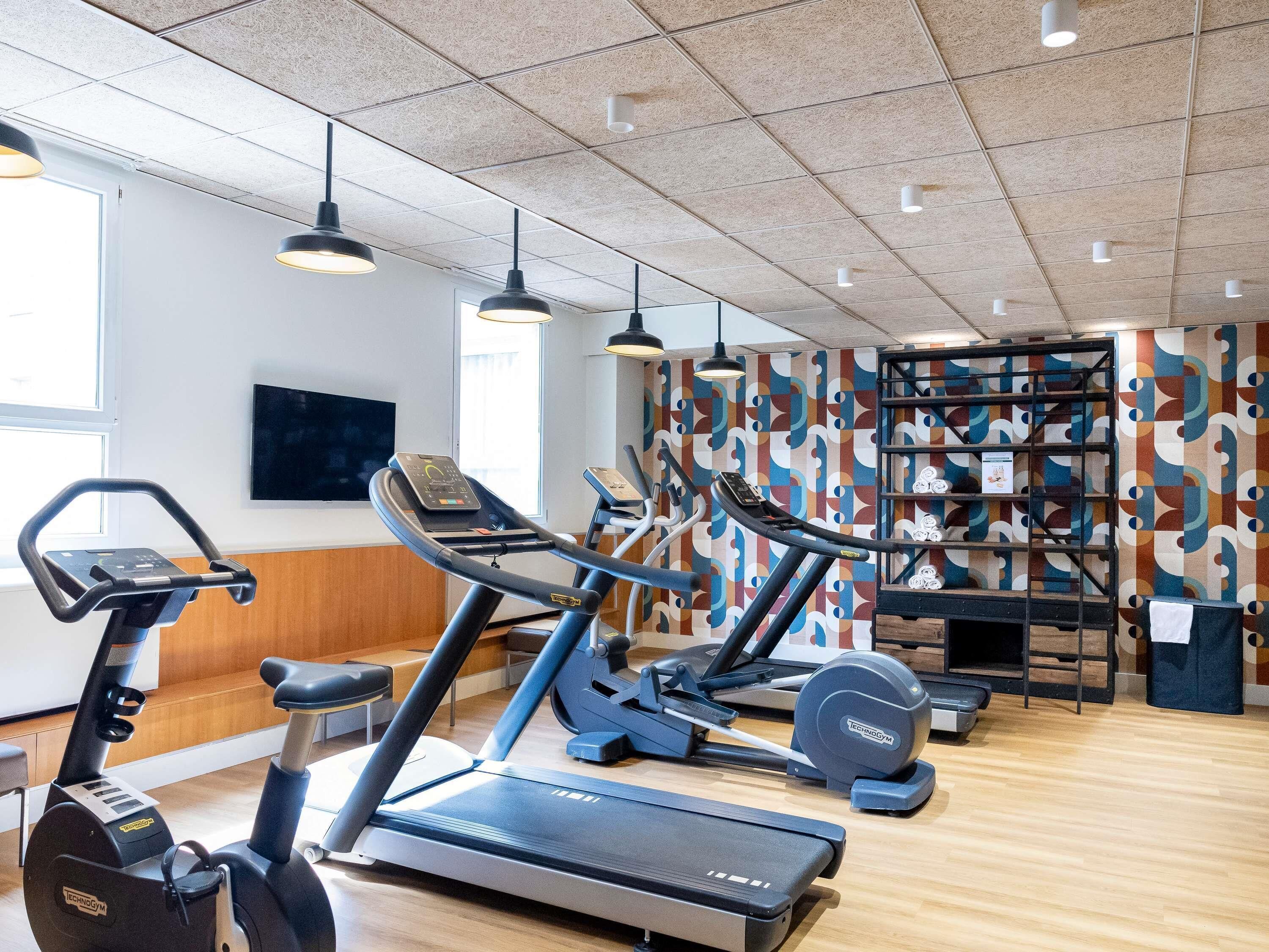 Et fitnessrum med træningsudstyr, fjernsyn og en mønstret væg.