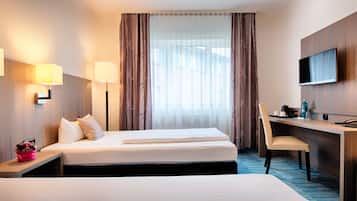 A hotel room with two beds, a desk, a chair, a TV, and a window with curtains.
