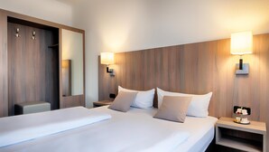 A hotel room with a large bed, two bedside tables, a nightstand, a mirror, and wall-mounted lamps. - ACHAT Hotel Bochum Dortmund (Bochum)