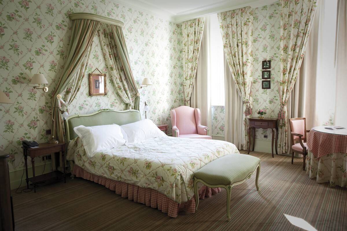 A bedroom with a four-poster bed, a desk, a chair, and a small table with a tablecloth.
