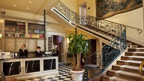 Un vestíbulo con mostrador de recepción, una escalera con barandillas ornamentadas y un mural grande en la pared.