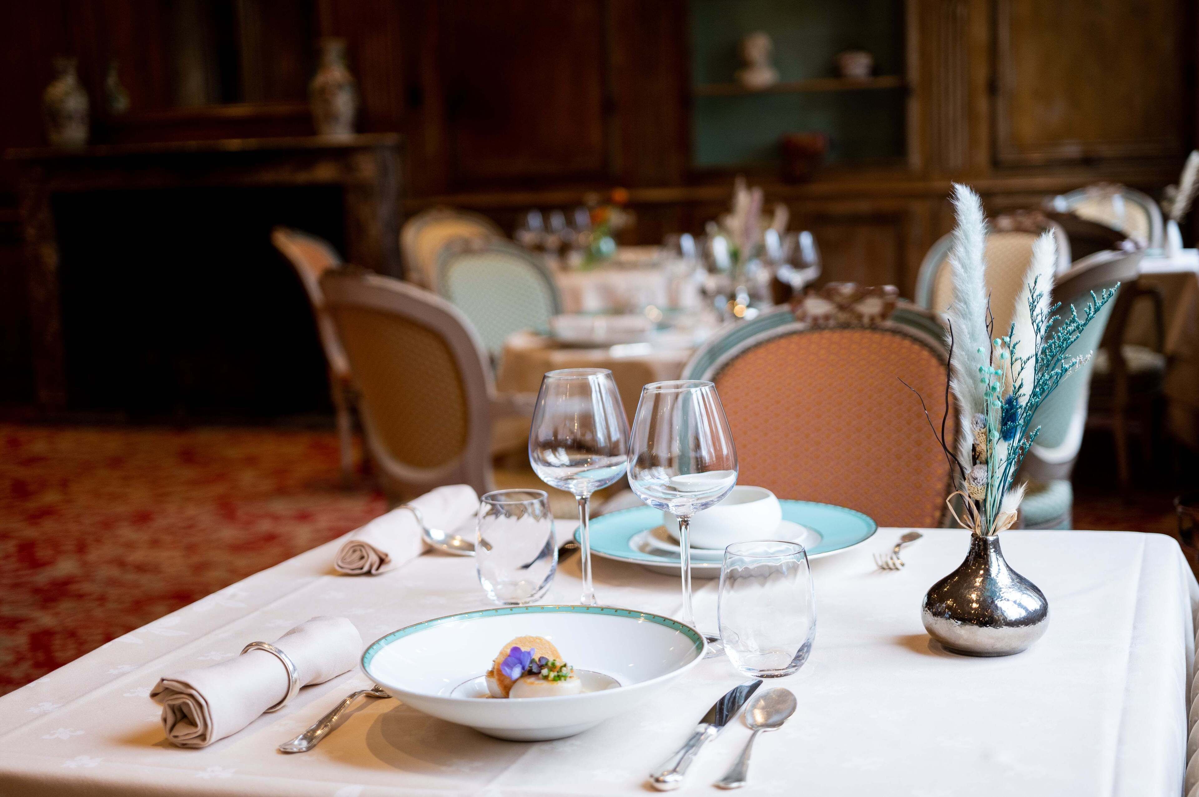A dining table set with plates, glasses, and cutlery, with a decorative vase and rolled napkins.
