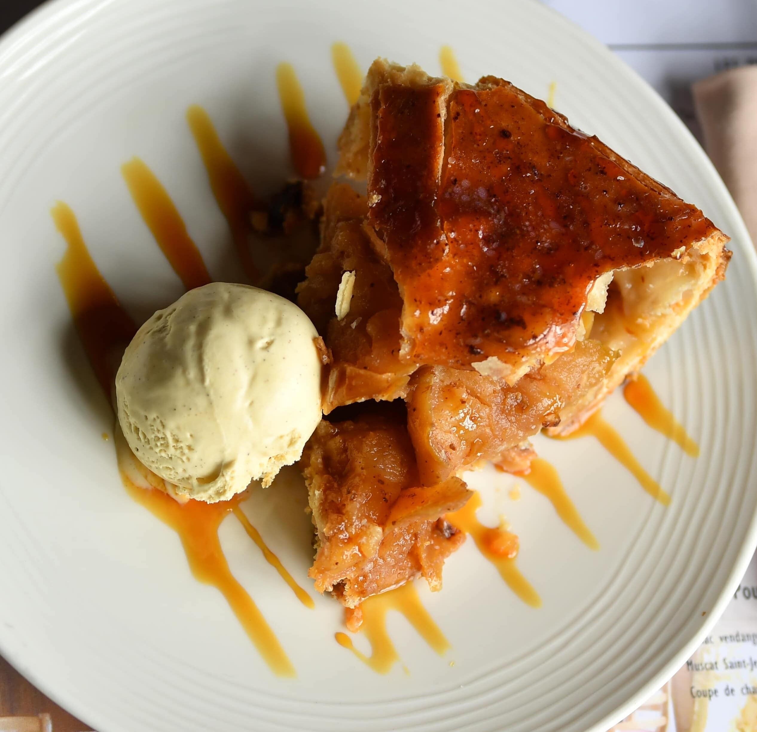 A dessert plate with a caramelized apple slice, a scoop of vanilla ice cream, and a drizzle of caramel sauce.