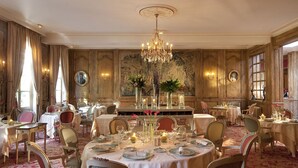 Un comedor formal con varias mesas dispuestas para el servicio, elegantes candelabros y decoración clásica.