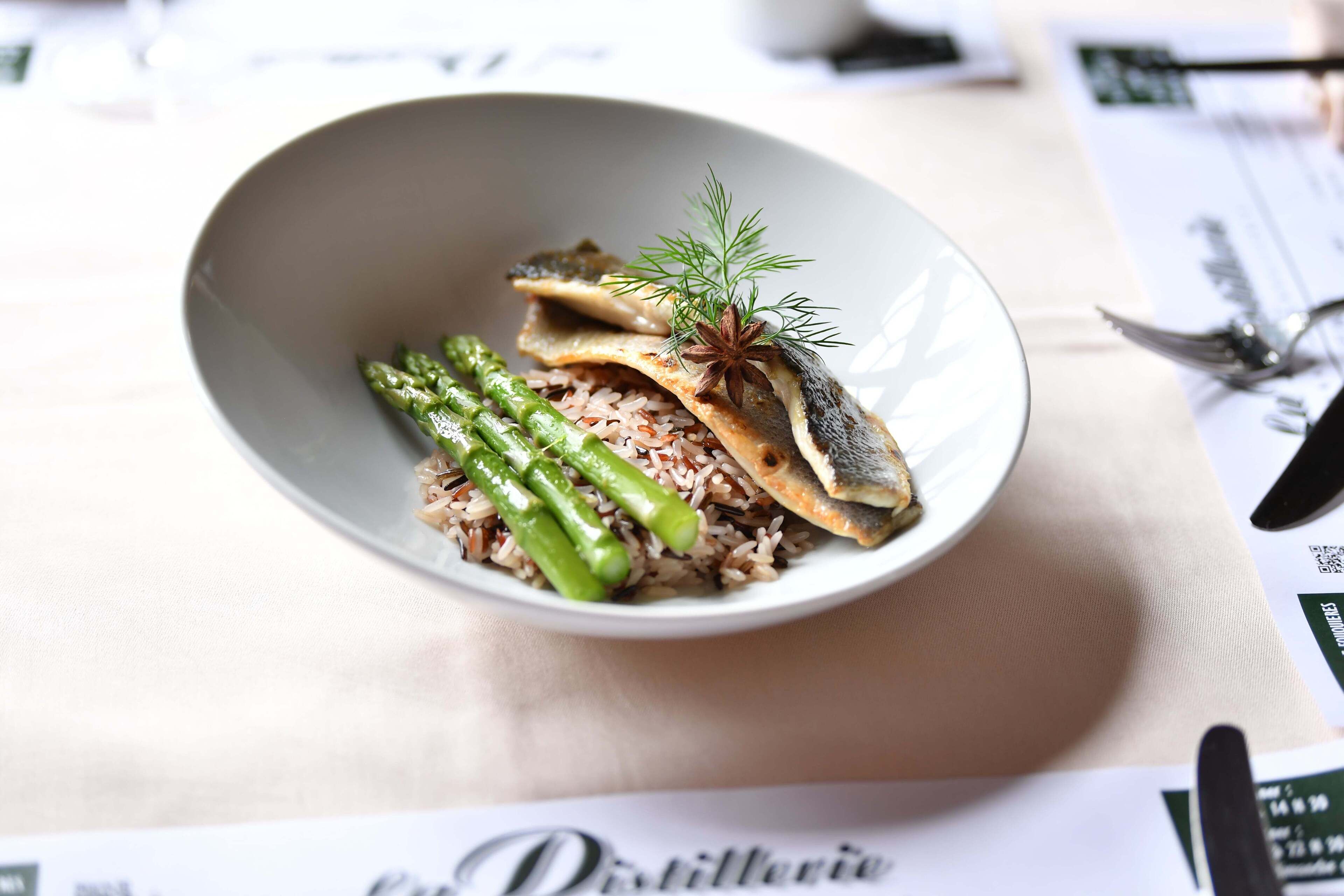 Un plat composé de riz, d’asperges vertes et de poisson, agrémenté d’une branche d’aneth et d’une étoile de badiane.