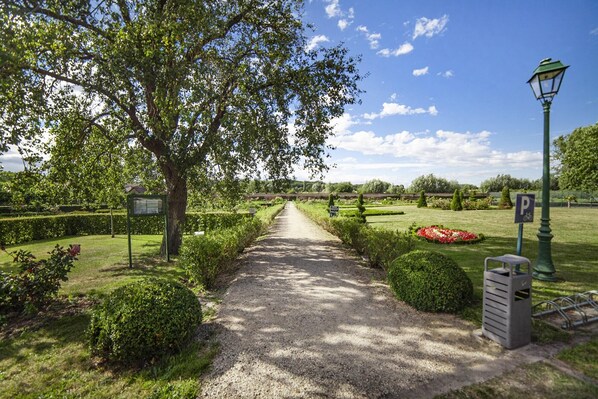 A gravel path leading through a park with a signboard, a bicycle parking area, and a lamp post. - La Chartreuse Du Val St Esprit (Gosnay)
