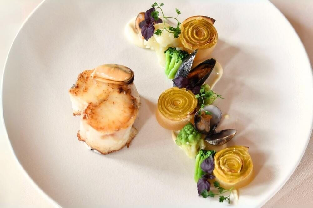Un plato de comida con vieiras a la plancha, brócoli y corazones de alcachofa.