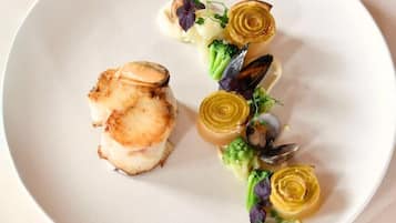 Un plato de comida con vieiras a la plancha, brócoli y corazones de alcachofa.