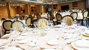 A banquet hall with multiple round tables set for dining, each with white tablecloths, silverware, and clear glassware.