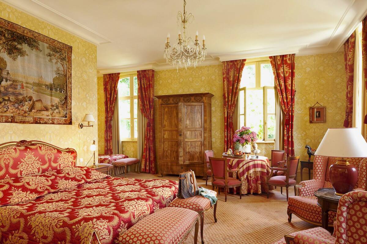 A room with a large bed, a wooden cabinet, a dining table with chairs, and a chandelier.