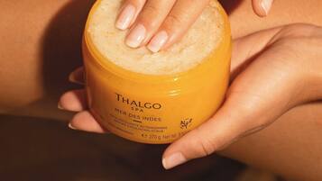 Iemand houdt een pot Thalgo spa gember exfoliërende scrub vast.
