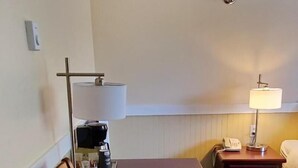 Habitación de hotel con una mesa de madera, una silla, una lámpara, una mesita de noche con lámpara y una cama.