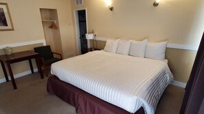 A hotel room with a large bed, a bedside table, a chair, and a wardrobe. - Comox Valley Inn & Suites (Courtenay)